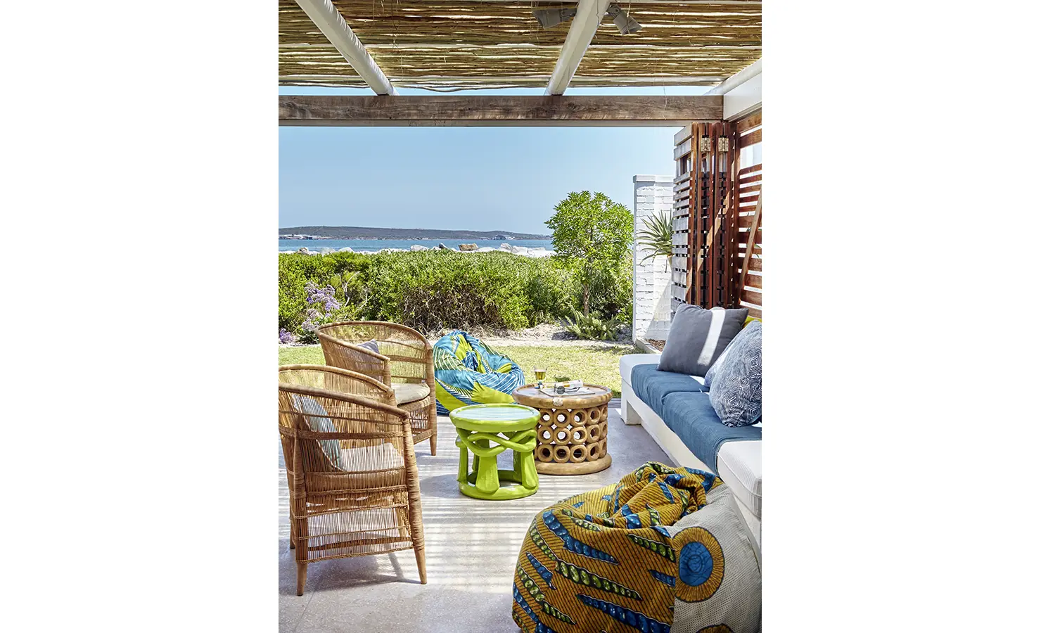 Perfect Hideaways: A relaxed outdoor lounge under a rustic pergola, with woven chairs, colourful bean bags, and a comfortable built-in bench overlooking the ocean. Blue Lagoon, Langebaan.