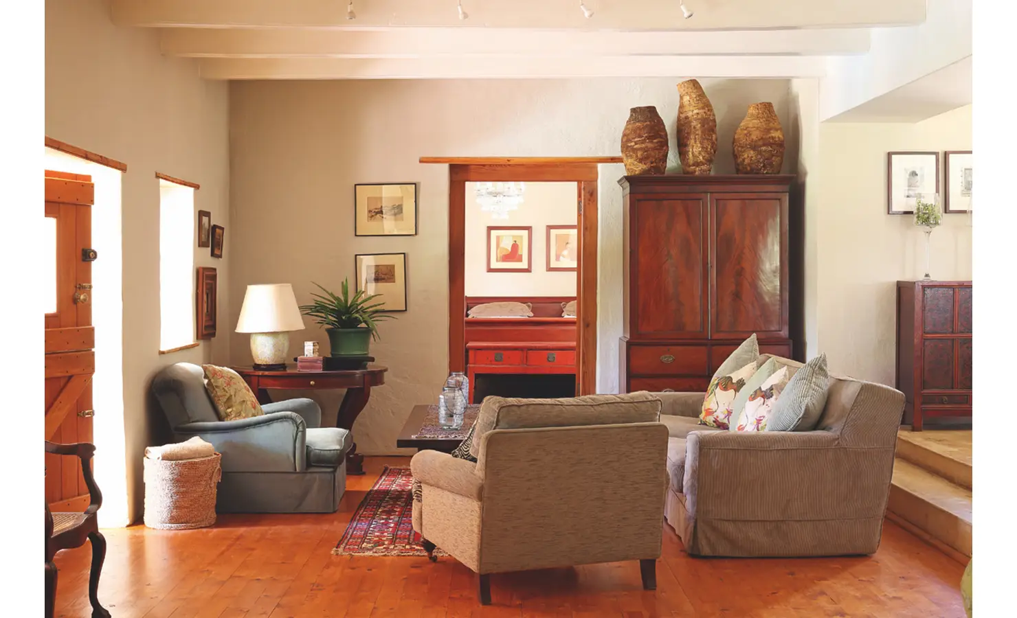 Joubertsdal living room with a low ceiling furnished with warm colours reflective in the soft beige sofa, blue armchairs and dark wooden coffee table and cabinet.