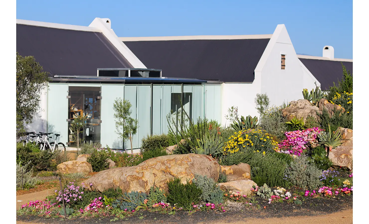 Perfect Hideaways: A contemporary glass-walled structure merges with the traditional Cape Dutch architecture, set within a vibrant rock garden filled with indigenous plants and colourful flowers. Babylonstoren, Franschhoek.