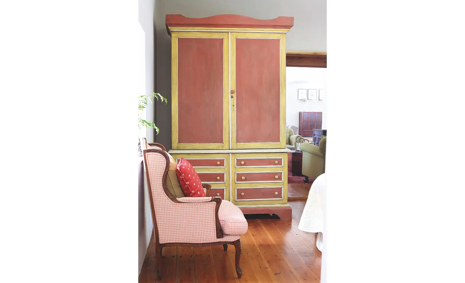 Red and yellow wooden cabinet complimenting the white and pink checkered armchair. Joubertsdal.