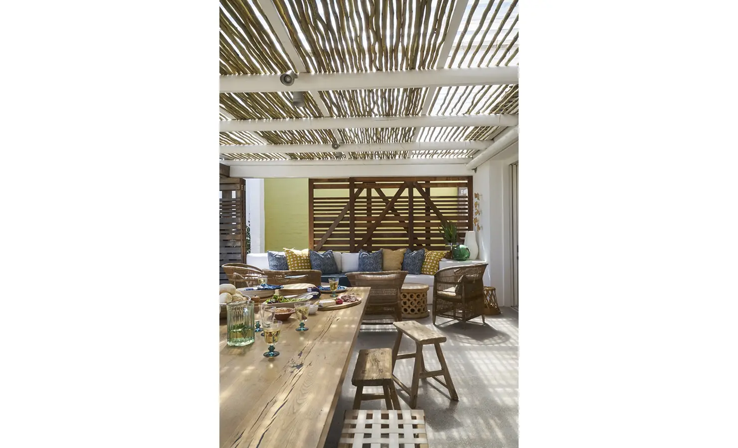 Perfect Hideaways: A stylish covered patio with a long dining table, wicker chairs, and a cosy built-in sofa adorned with blue and yellow cushions, creating a perfect spot for entertaining. Blue Lagoon, Langebaan.