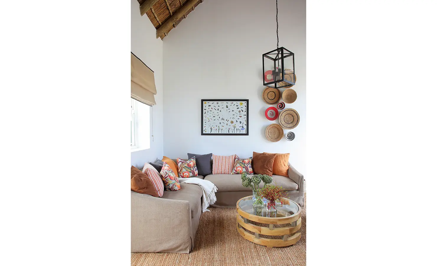 Perfect Hideaways: A cosy and inviting living space featuring a thatched ceiling, earth-toned sofas adorned with colourful cushions, and an eclectic collection of woven baskets on the wall. A warm and rustic retreat perfect for unwinding. Penhill Fruit Barn, Nuy Valley.