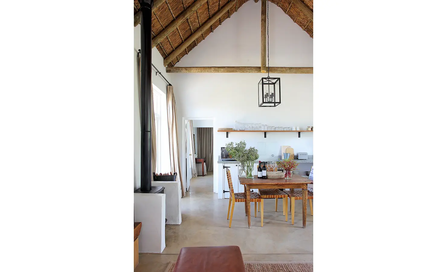 Perfect Hideaways: An airy open-plan kitchen and dining space with high thatched ceilings, wooden beams, and a rustic farmhouse table. A fireplace adds warmth to the space, creating a perfect balance of modern comfort and country charm. Penhill Fruit Barn, Nuy Valley.