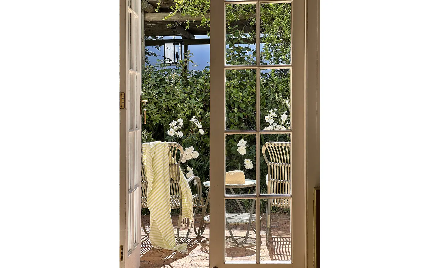 Perfect Hideaways: A view through French doors of a patio with wicker chairs, surrounded by blooming white flowers. Penhill Manor House, Nuy Valley.