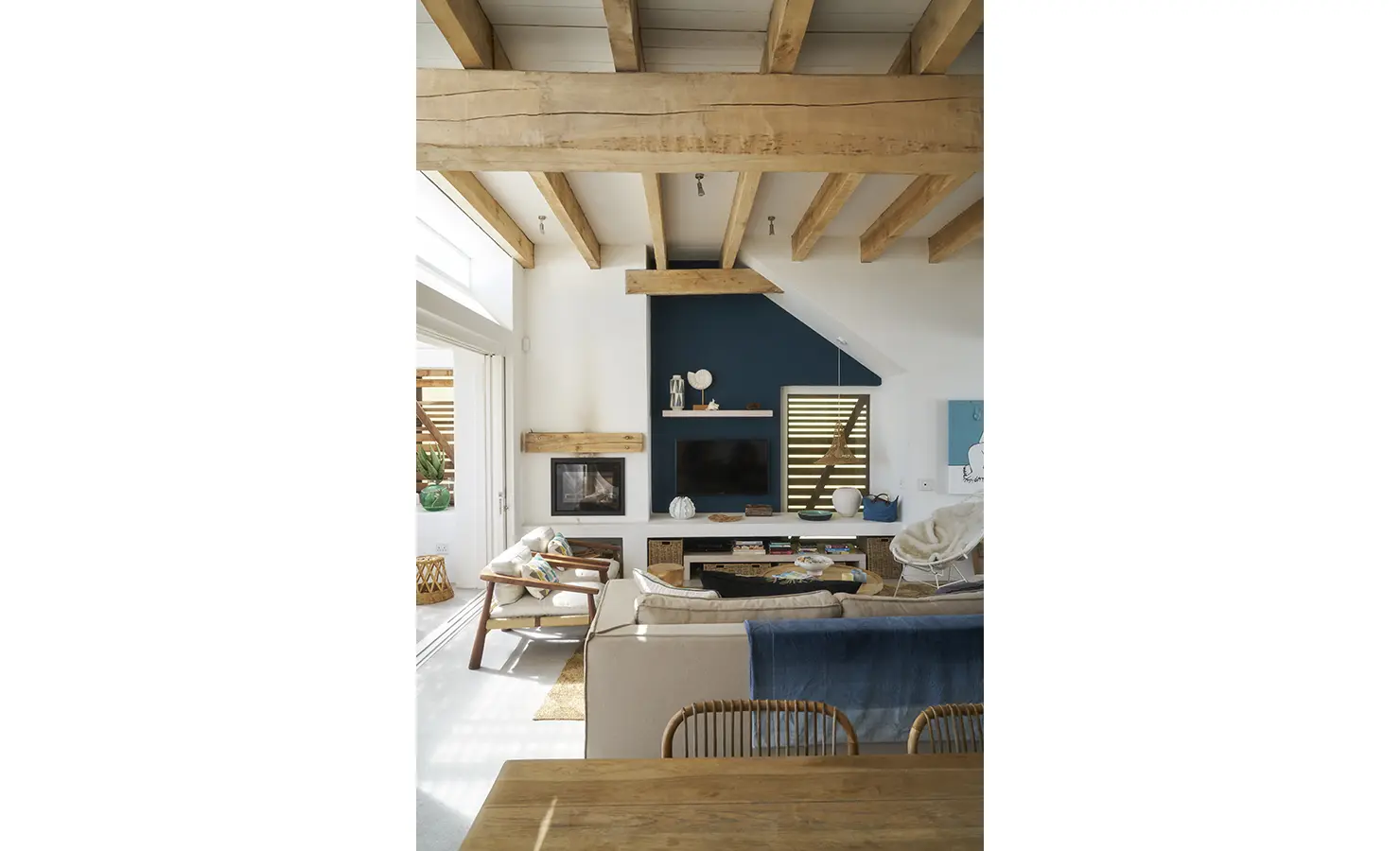 Perfect Hideaways: A cosy yet elegant lounge area with high ceilings, wooden beams, and a fireplace, blending natural textures with deep blue tones for a relaxed coastal ambiance. Blue Lagoon, Langebaan.
