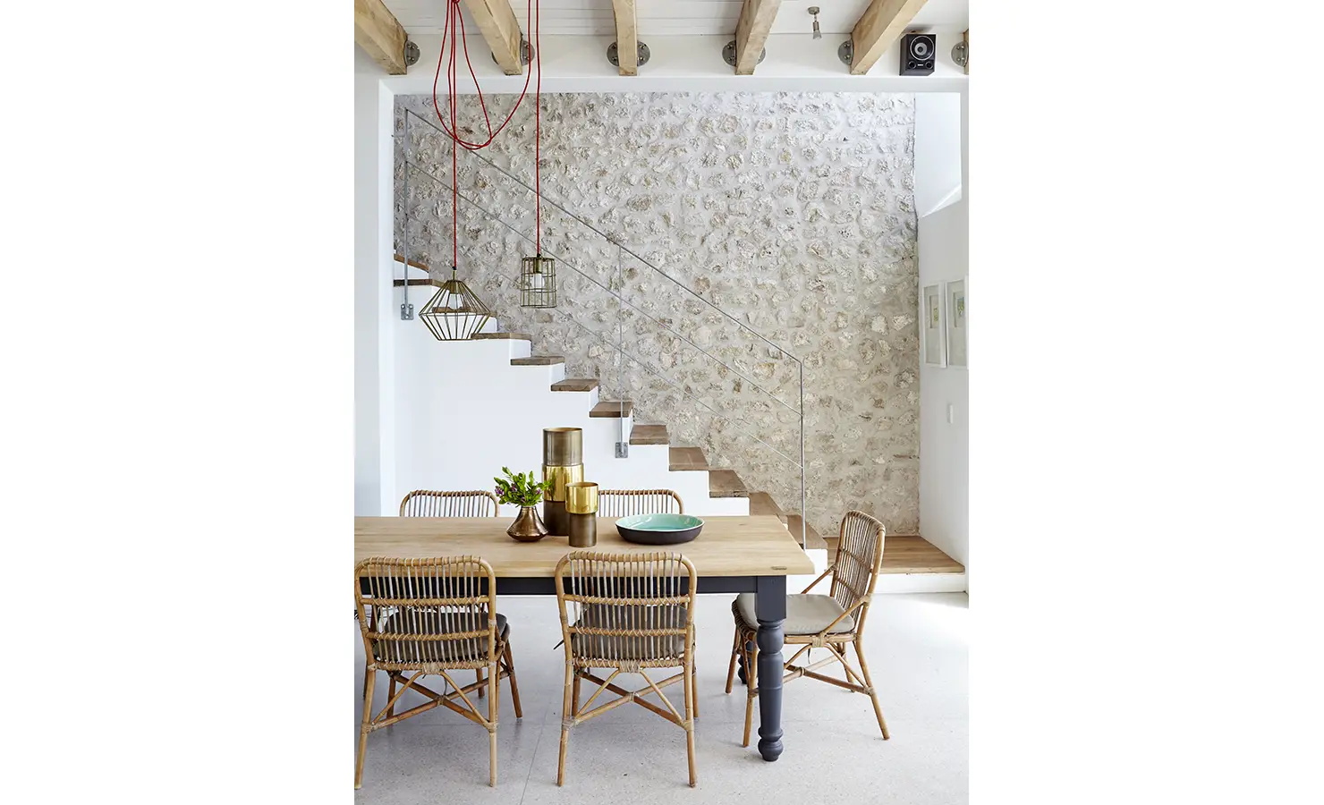 Perfect Hideaways: A minimalist yet inviting dining space with a solid wooden table, rattan chairs, and contemporary pendant lighting against a textured stone wall and floating staircase. Blue Lagoon, Langebaan.
