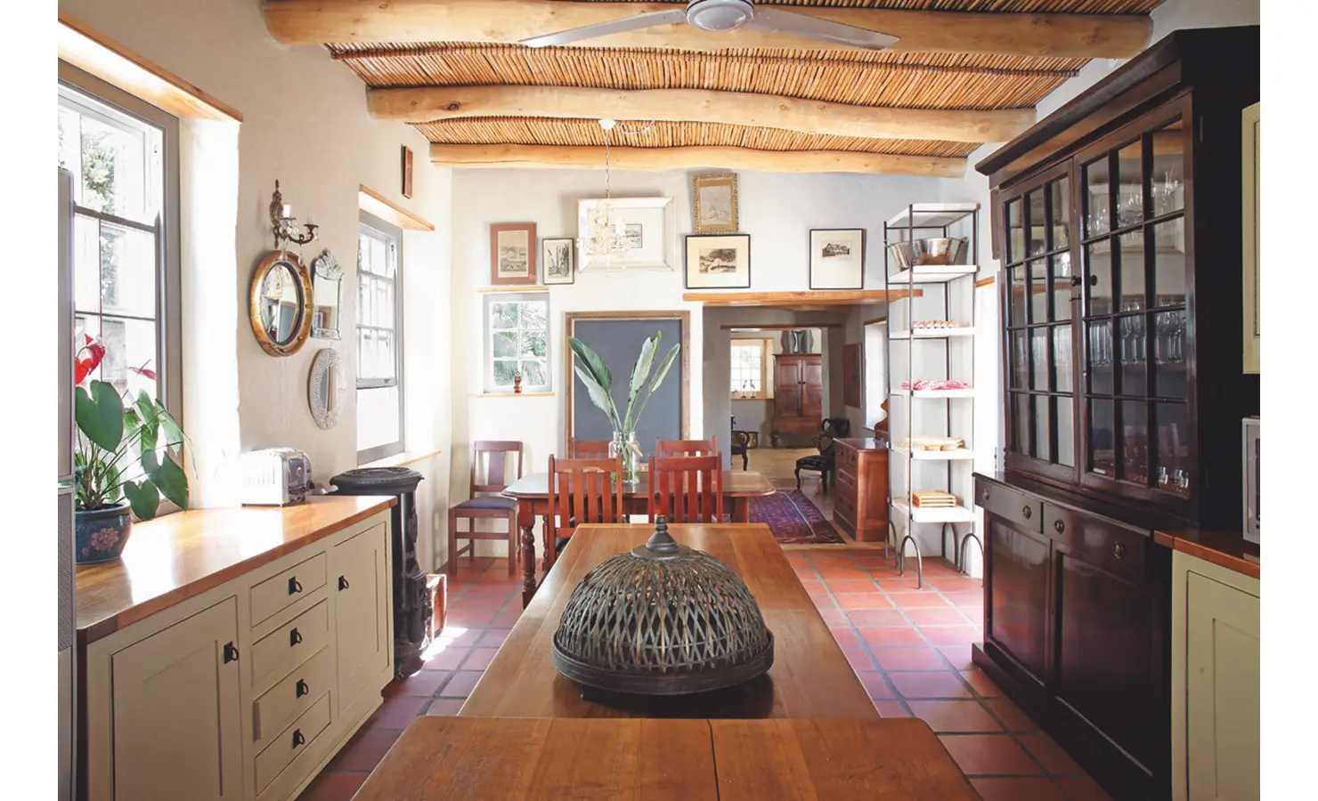 Joubertsdal kitchen with bamboo ceiling, cream walls decorated in art, terracotta floors, and beige cabinets with sleek wooden counter tops.