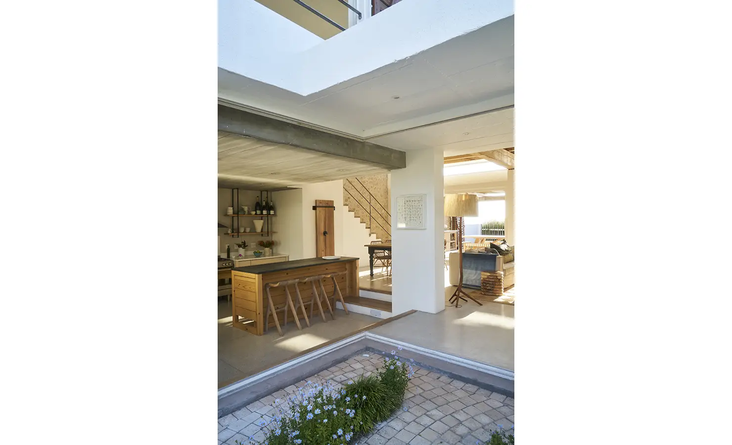 Perfect Hideaways: A seamless indoor-outdoor living space, where the kitchen opens up to a sunlit courtyard with lush greenery and a rustic wooden dining area. Blue Lagoon, Langebaan.