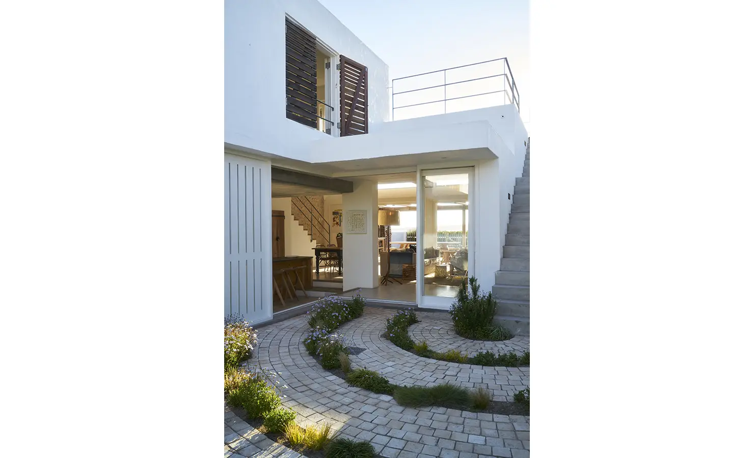 Perfect Hideaways: A striking modern coastal home with a white facade, wooden shutters, and a lush courtyard with curved stone pathways leading to the inviting interior spaces. Blue Lagoon, Langebaan.