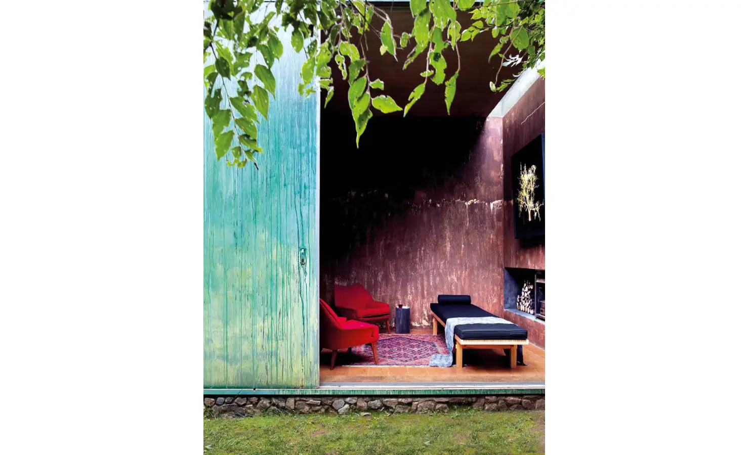 Perfect Hideaways: A striking lounge space with rich earth-toned walls, deep blue daybeds, and bold red armchairs, framed by a large, weathered green sliding door. The Pavilion, Cradle of Human Kind.