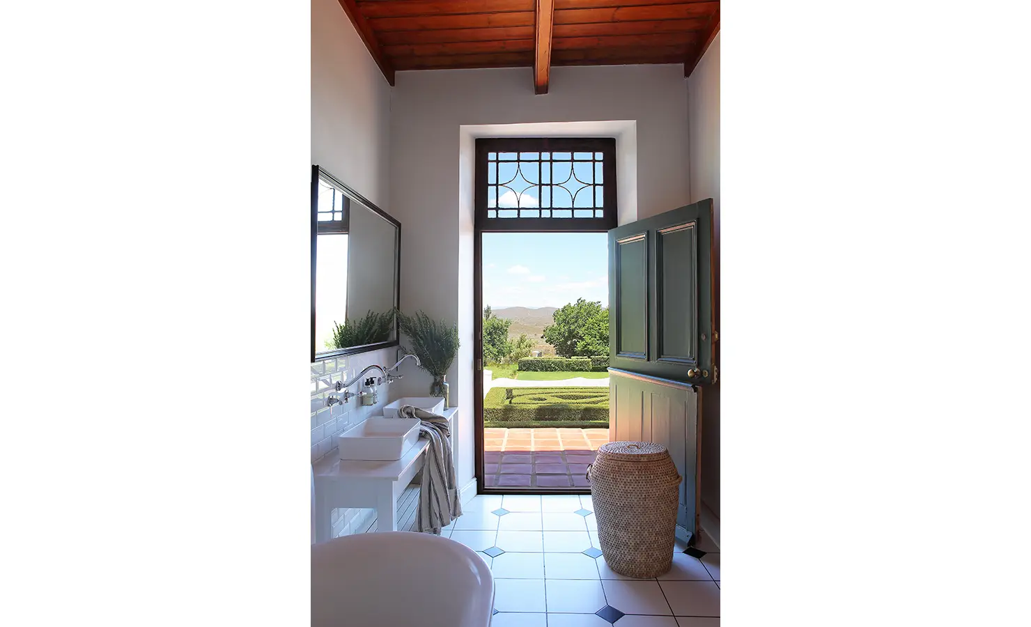 Perfect Hideaways: A bright bathroom with white tiled walls, a basin, and a doorway leading to a scenic view of the garden and hills beyond. Penhill Manor House, Nuy Valley.
