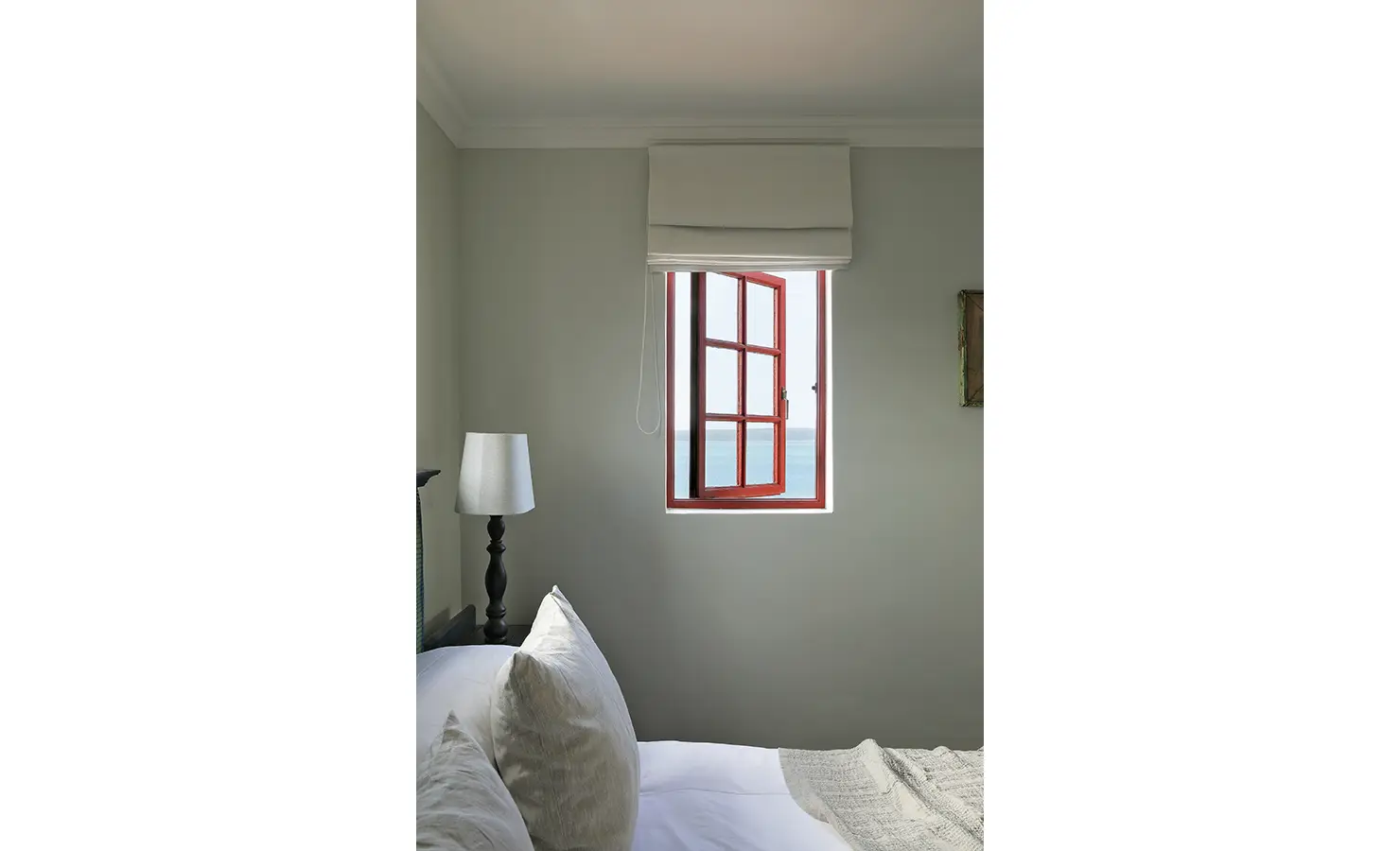 Perfect Hideaways: A peaceful bedroom with a red-framed window flung open to reveal sea views, soft grey walls, and plush white linens beneath. Churchhaven, Fynbos.