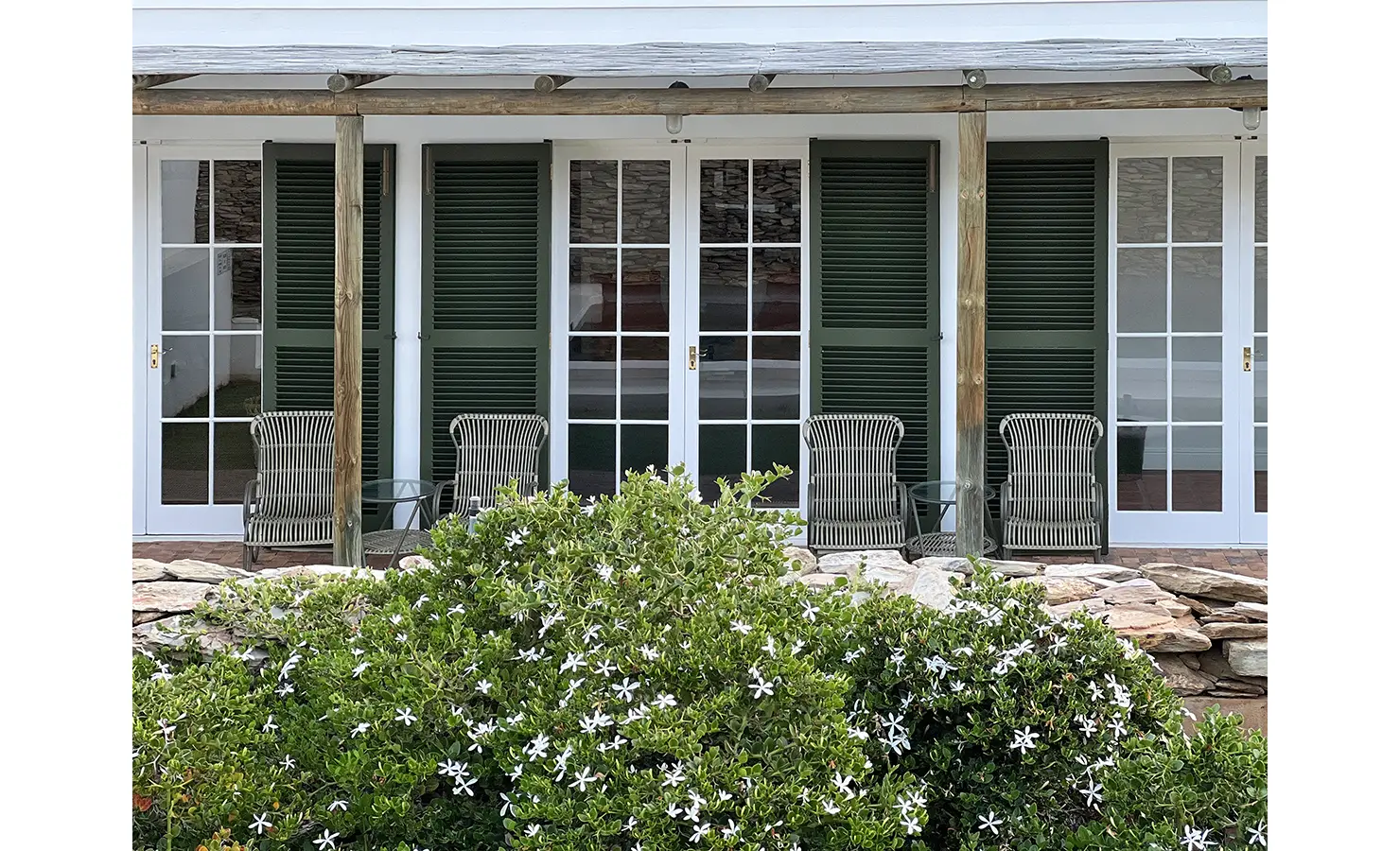 Perfect Hideaways: An inviting patio with wicker chairs framed by French doors and flourishing jasmine bushes in bloom. Penhill Manor House, Nuy Valley.