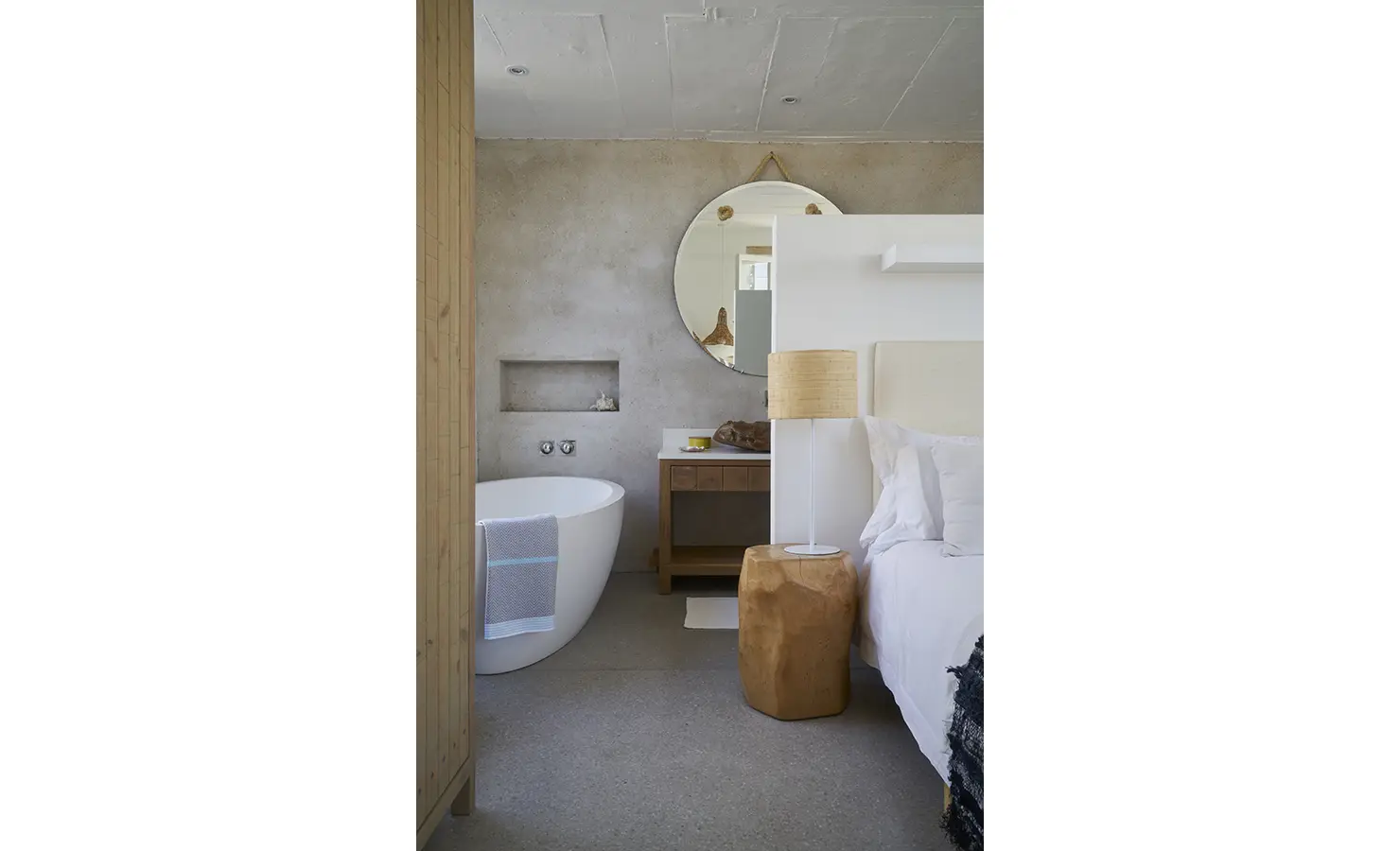 Perfect Hideaways: A stylish en-suite bedroom featuring a freestanding bathtub, textured concrete walls, and warm natural wood elements for a modern coastal retreat. Blue Lagoon, Langebaan.