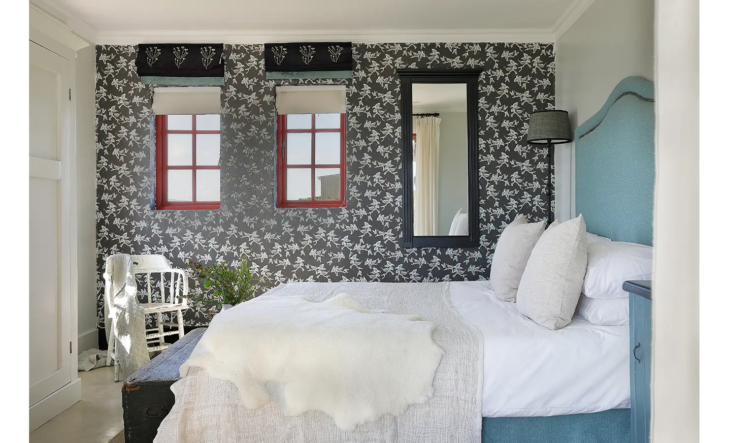 Perfect Hideaways: A characterful bedroom with a bold floral feature wall, red-trimmed windows, and an upholstered turquoise headboard offers a cheerful yet elegant retreat. Churchhaven, Fynbos.