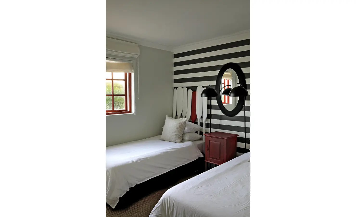 Perfect Hideaways: A playful nautical-themed twin bedroom with black and white striped walls, oar-shaped headboards and a bold red nightstand beneath oval mirrors and black lamps, Churchhaven, Fynbos.