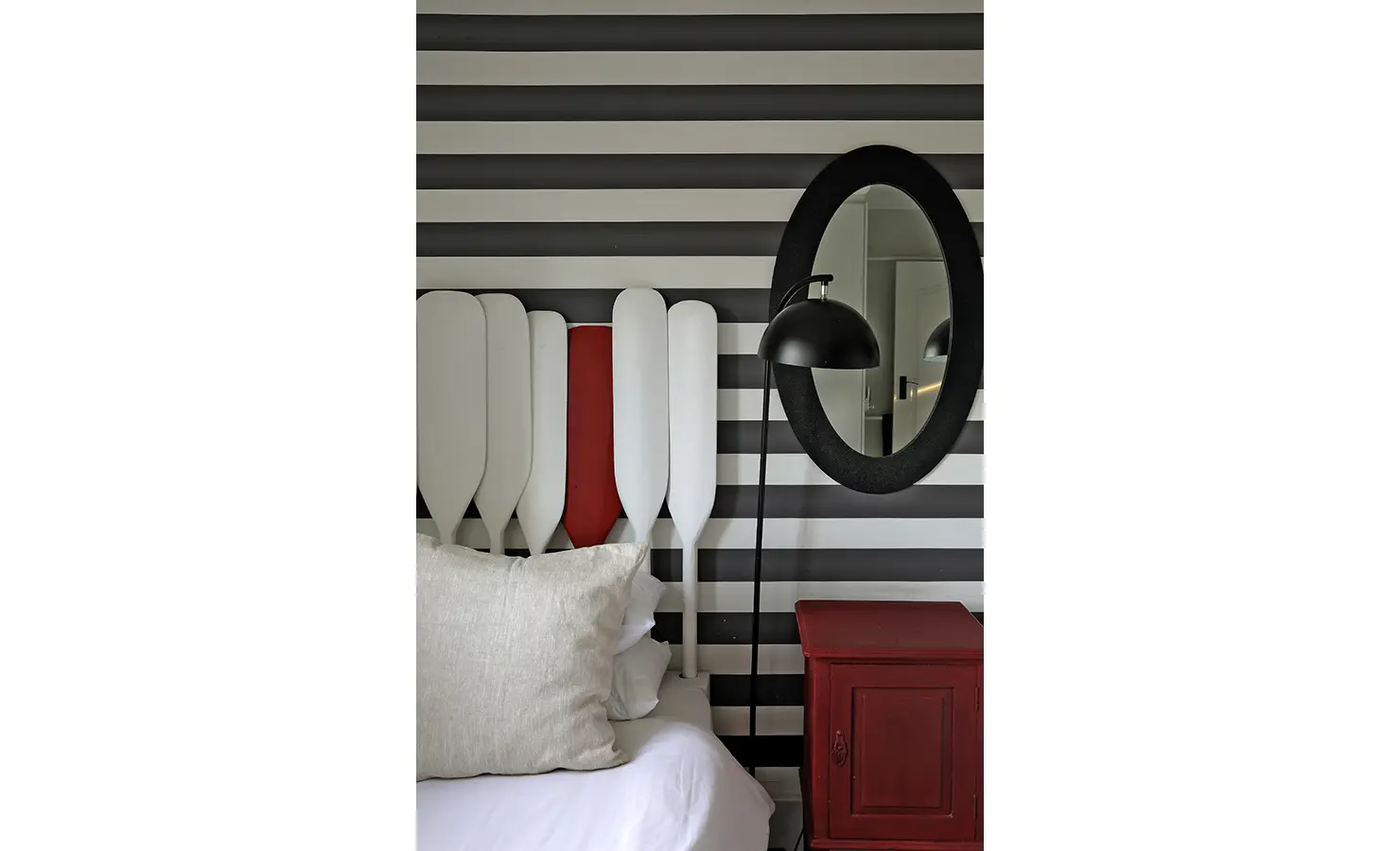 Perfect Hideaways: A close-up of a striking bed with a creative oar headboard in white and red, backed by bold monochrome stripes and paired with a black-framed mirror and rustic red nightstand, Churchhaven, Fynbos.