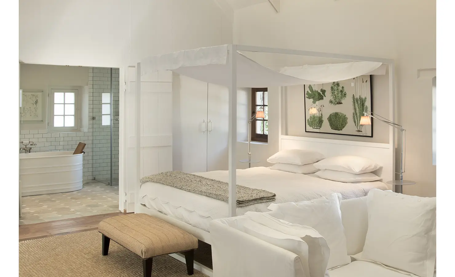 Perfect Hideaways: A charming bedroom featuring a four-poster bed with soft drapery, botanical artwork, and an en-suite bathroom with a freestanding tub, blending rustic elegance with modern comfort. Babylonstoren, Franschhoek.