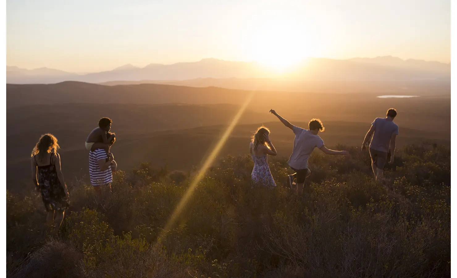 Perfect Hideaways: A group of people enjoying a sunset hike on a ridge, silhouetted by the warm glow of the sun over expansive valleys. Penhill Manor House, Nuy Valley.