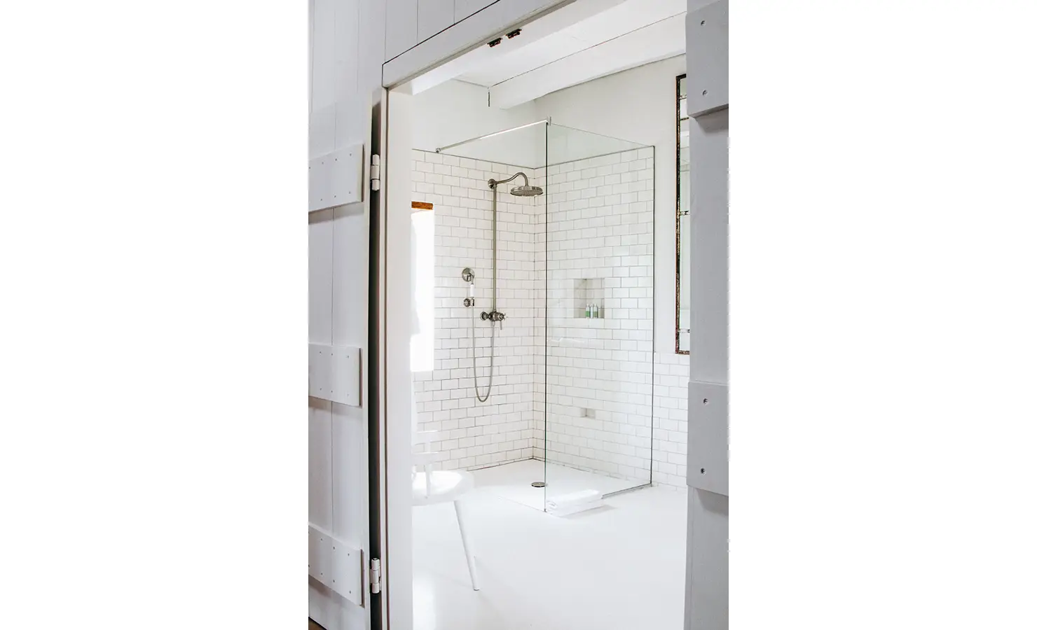 Perfect Hideaways: A minimalist walk-in shower framed by rustic wooden doors, featuring white subway tiles, a rain shower head, and an airy, open design. Babylonstoren, Franschhoek.