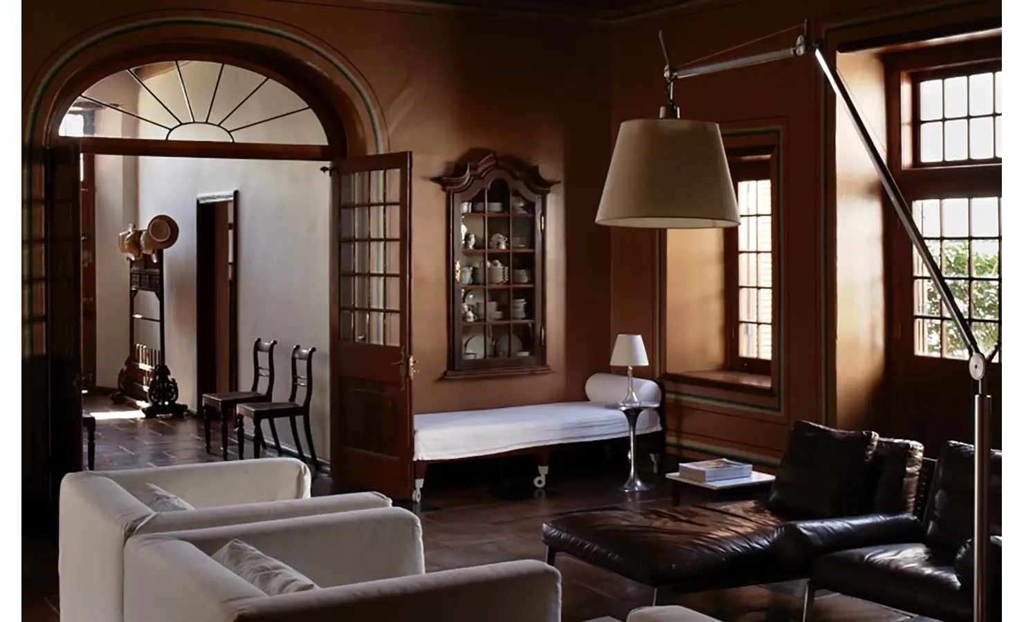 Perfect Hideaways: A timeless sitting room with rich earth-toned walls, antique furniture, and soft lighting, creating an intimate and sophisticated atmosphere. Babylonstoren, Franschhoek.
