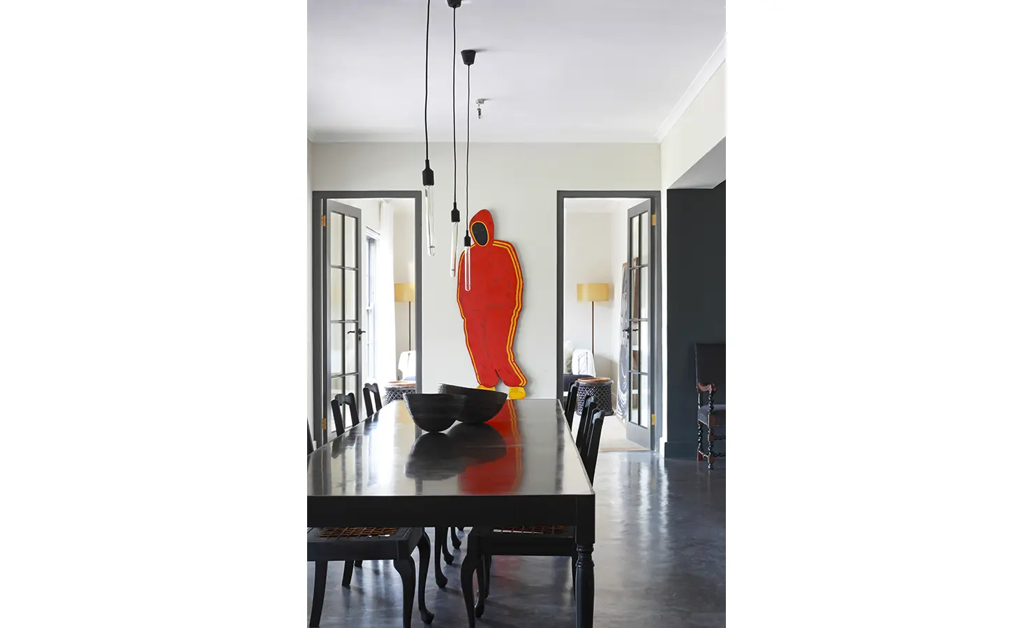 Large dark wooden dining table and chairs with life size artwork of man in red sports tracksuit. Koko House