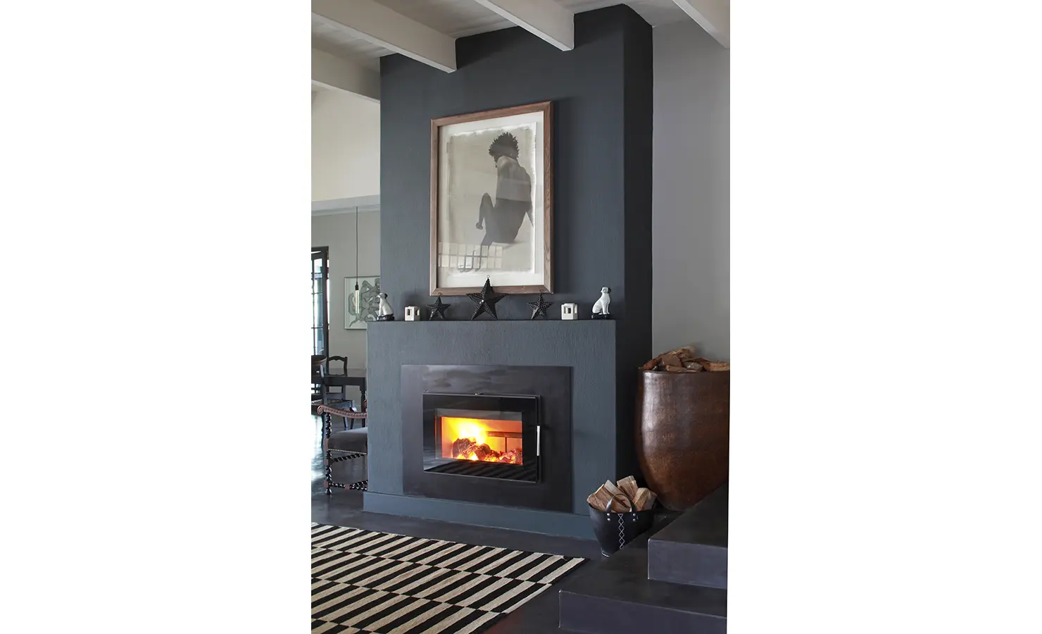 Indoor wood burning fireplace against dark blue painted wall with contemporary portrait sketch. Koko House.