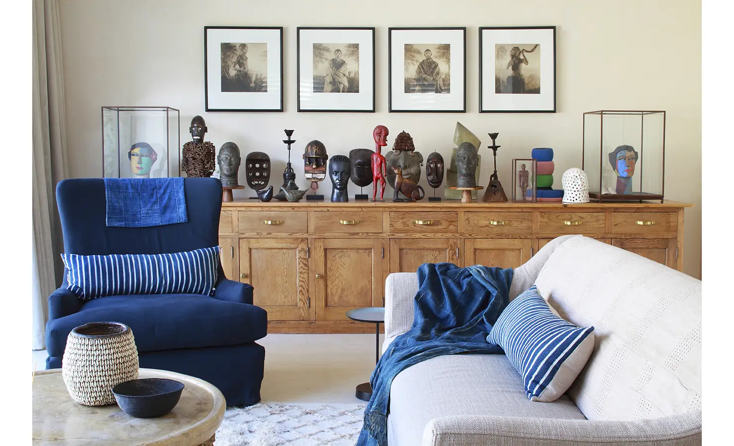 Blue and white couches with large wooden console and carved wooden figurines and masks on display. Koko House.