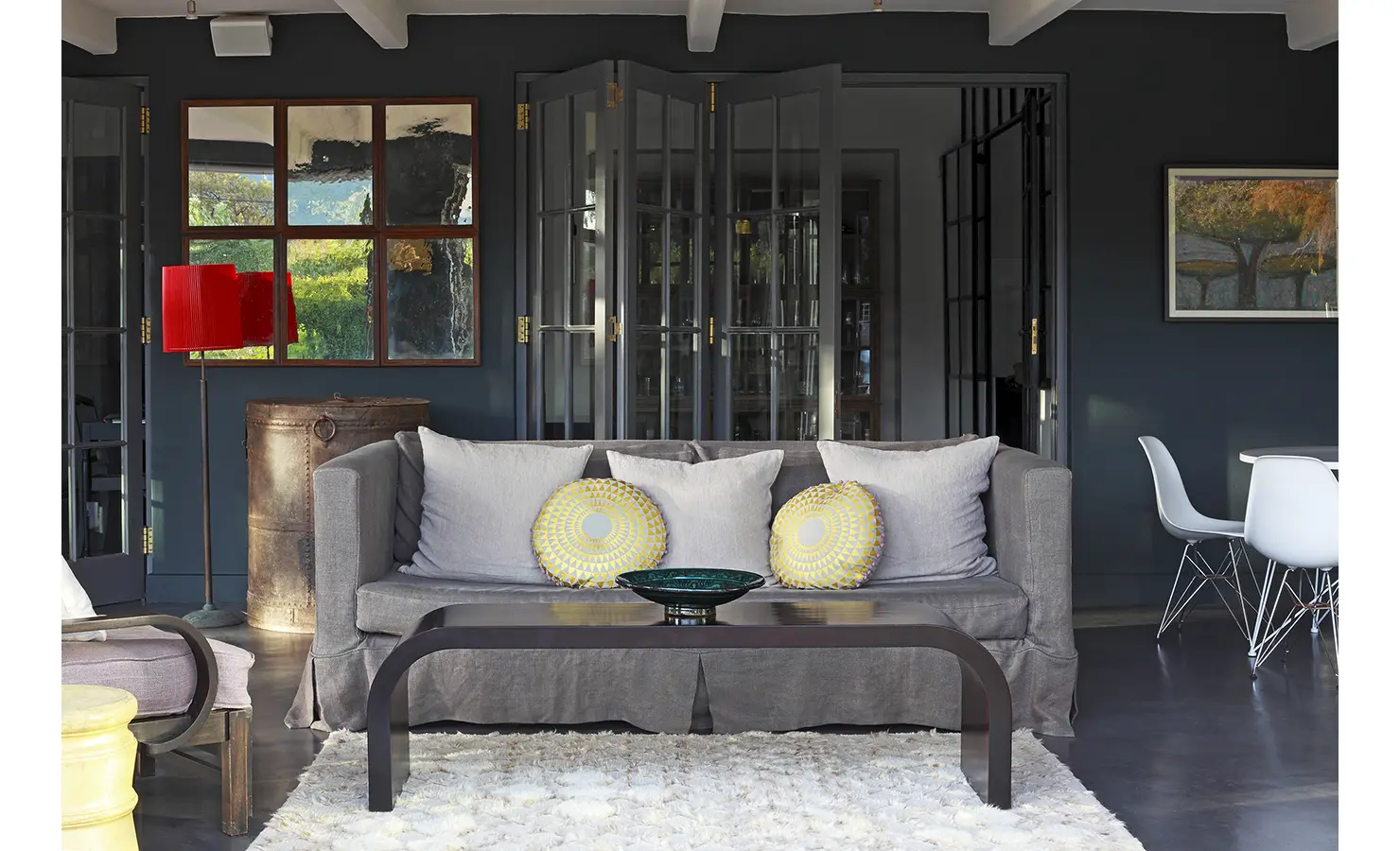 Grey couch, bright red lamp shade in a dark blue grey painted room with mirrors and stacking doors. Koko House.