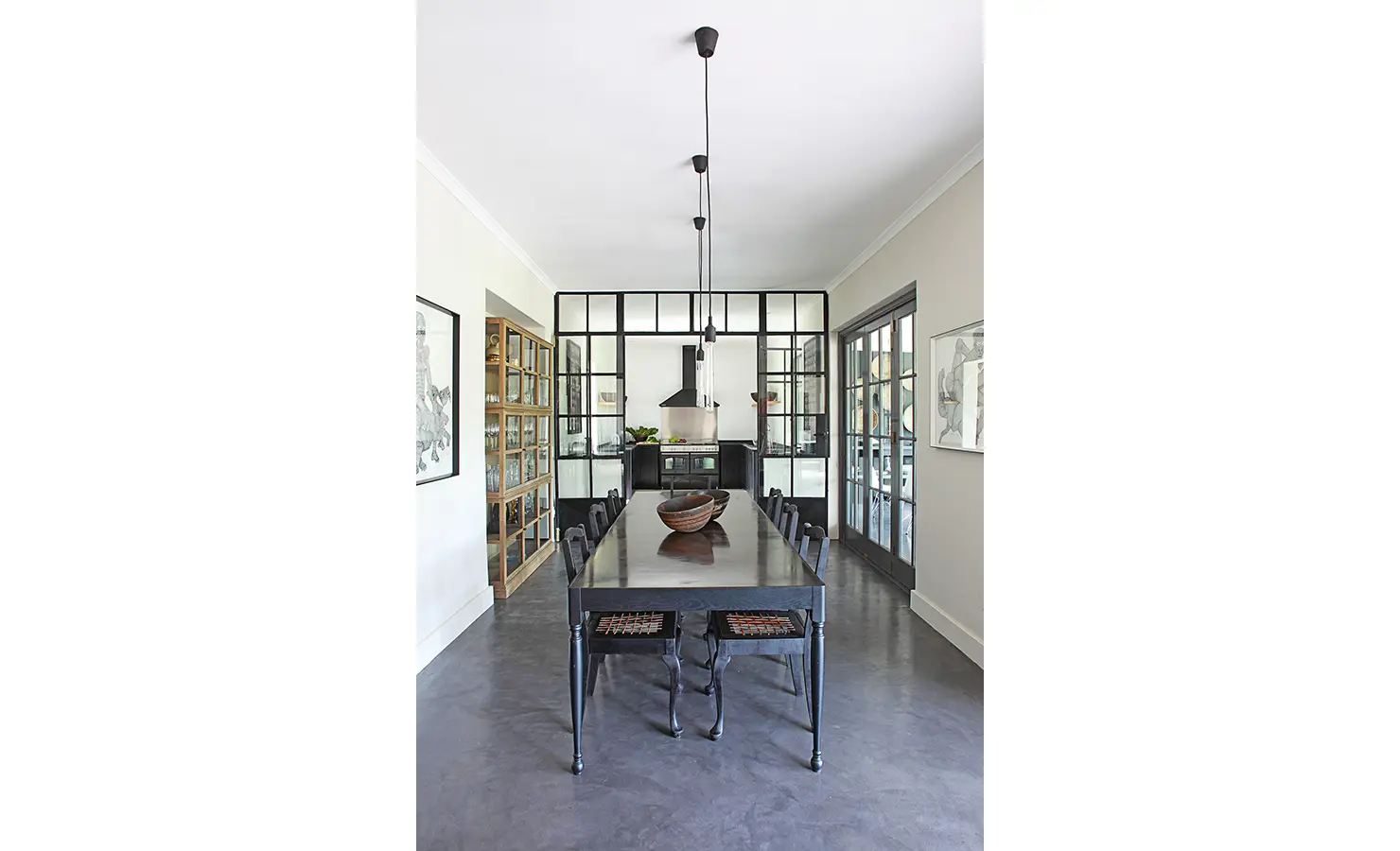 Large dark wooden dining table and chairs leading to small kitchen and surrounded by french pane glass doors. Koko House.