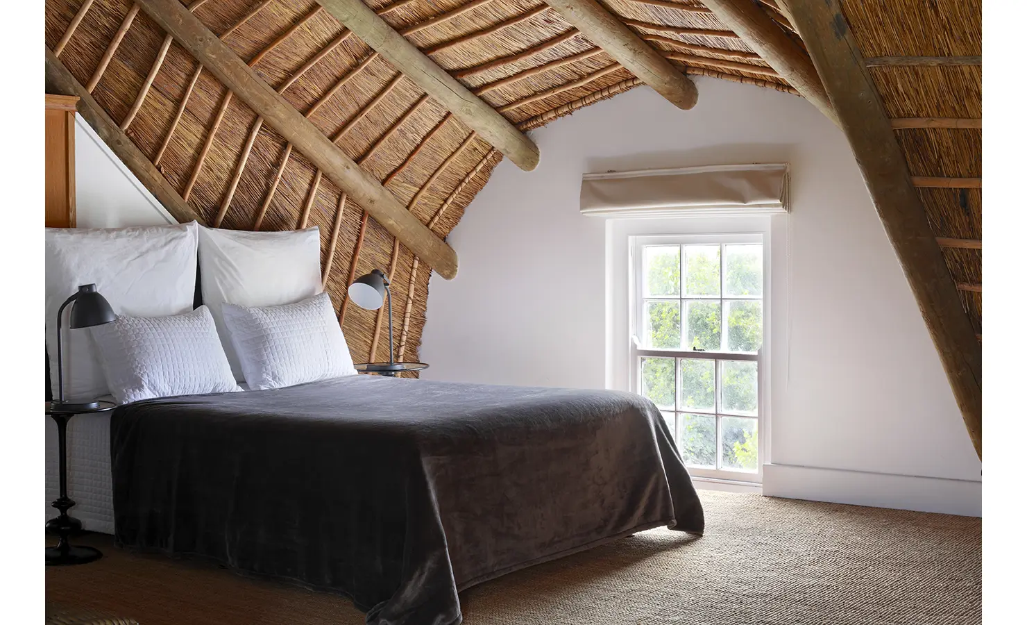 Loft bedroom with thatch ceiling and sash window. Koko House.