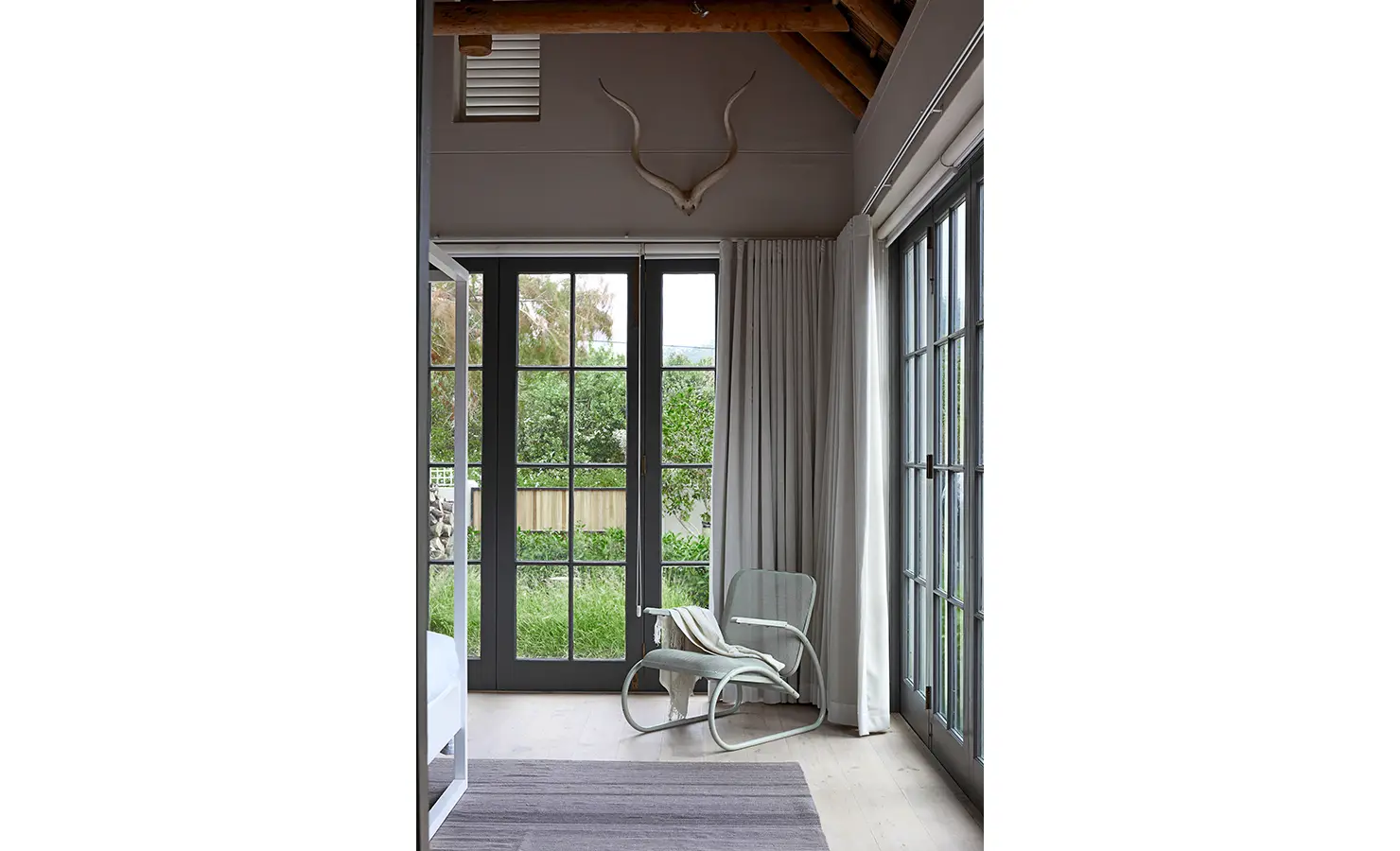 Bedroom view point with occasional corner chair looking out french pane doors onto garden. Koko House.