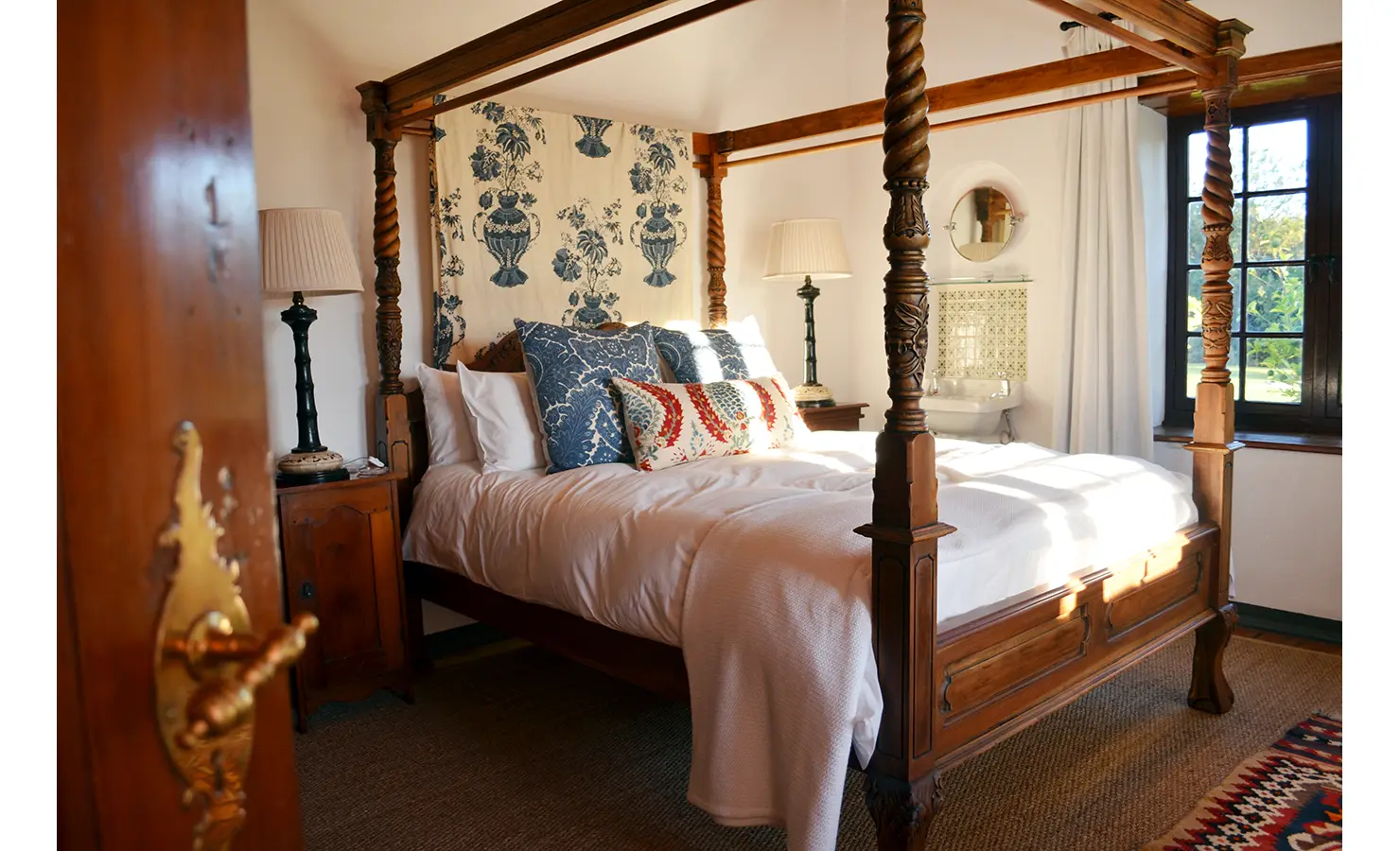 Perfect Hideaways: A serene bedroom with a four-poster wooden bed, ornate linens, and vintage furnishings, illuminated by natural light. Cottage 1685, Franschhoek.