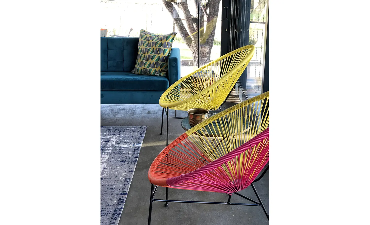 Perfect Hideaways: Brightly coloured string chairs in yellow and magenta add a playful pop of colour next to a velvet teal sofa, all set against sleek concrete flooring and glass walls. 22 Degrees East, Prince Albert.