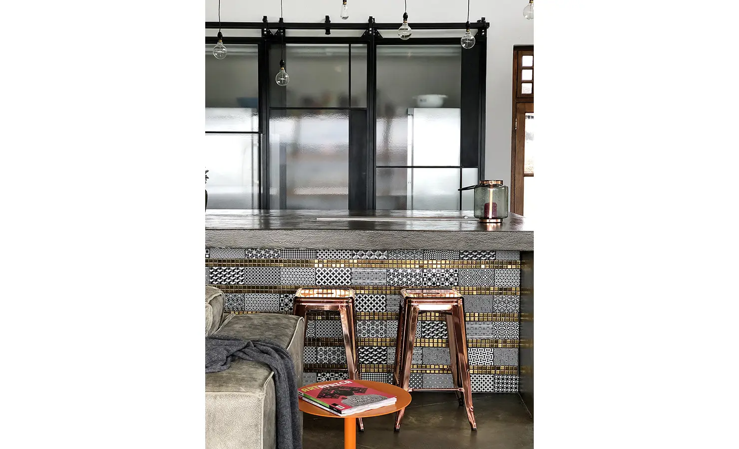 Perfect Hideaways: A closer look at the kitchen island reveals intricate patterned tiles in monochrome and metallics, with copper stools and minimalist lighting enhancing the contemporary style. 22 Degrees East, Prince Albert.
