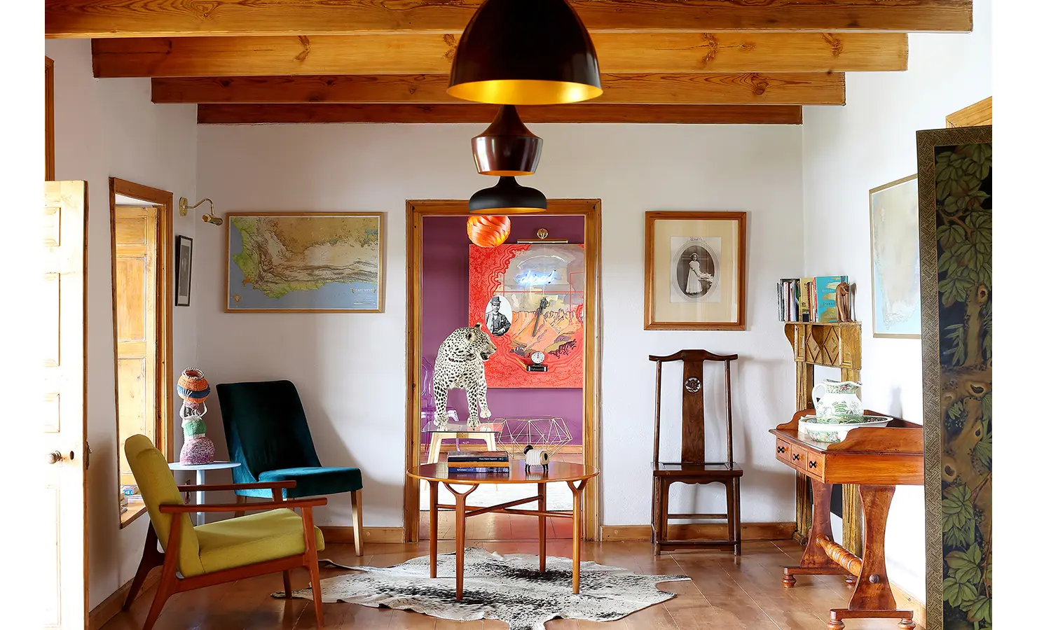 Perfect Hideaways: A vibrant hallway features eclectic furniture, maps, and playful art, with a bold pop of colour from an adjoining room displaying a striking leopard sculpture. 22 Degrees East, Prince Albert.