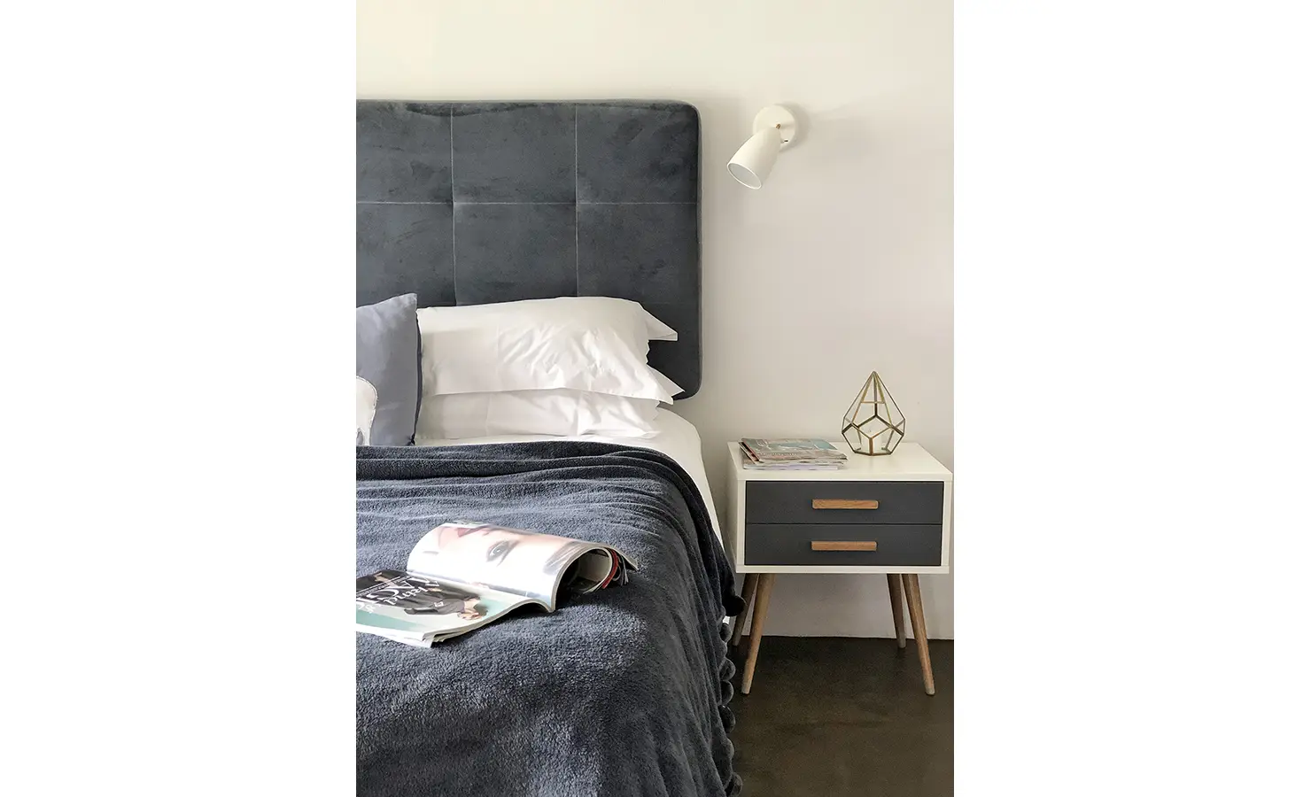 Perfect Hideaways: A cosy and contemporary bedroom with a charcoal tufted headboard and soft white linen is paired with a minimalist nightstand and geometric accent decor. 22 Degrees East, Prince Albert.