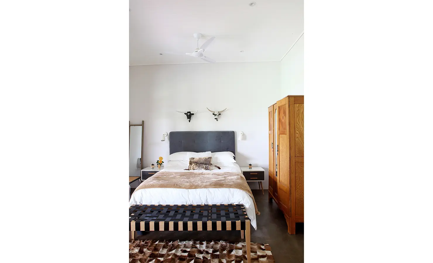 Perfect Hideaways: A modern rustic bedroom combines soft textures and raw elements, with animal skull wall decor, a sleek upholstered bed, and a statement wooden wardrobe. 22 Degrees East, Prince Albert.