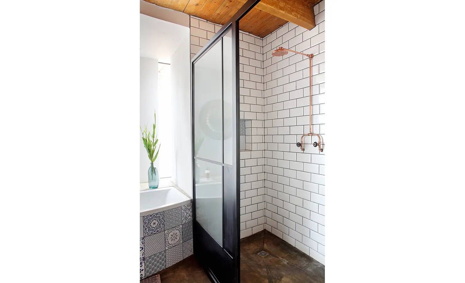 Perfect Hideaways: A minimalist shower features crisp white subway tiles and striking copper pipe fixtures, set beneath a natural wood ceiling with a black-framed glass partition. 22 Degrees East, Prince Albert.