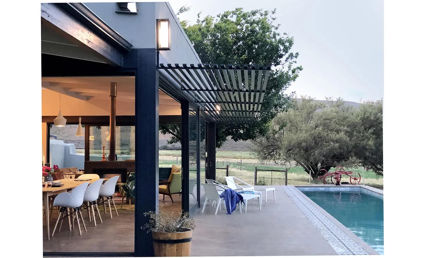 Perfect Hideaways: The home’s exterior showcases modern lines and glass walls opening onto a poolside terrace, with dining and lounging areas immersed in the Karoo landscape. 22 Degrees East, Prince Albert.