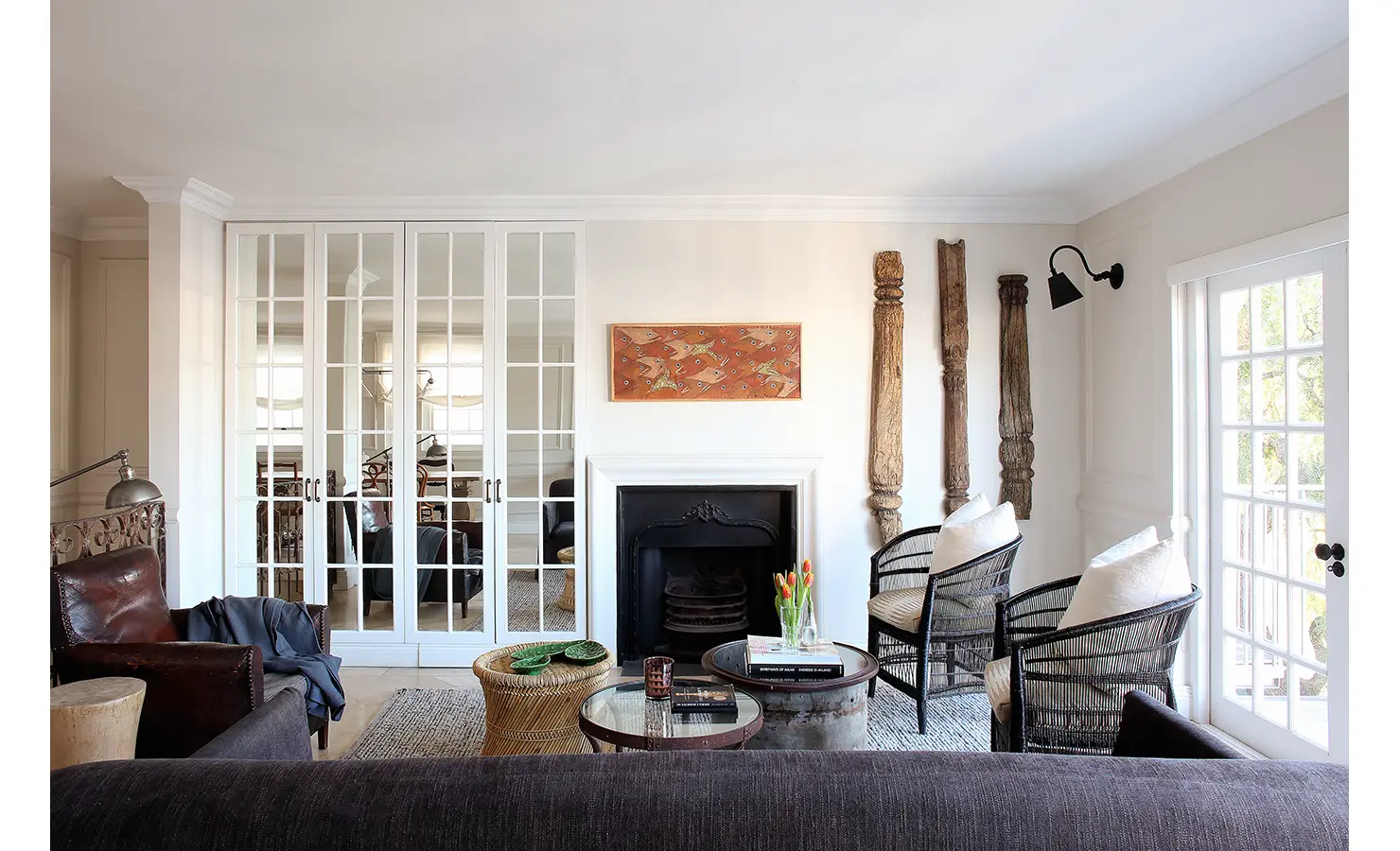 Perfect Hideaways: Cosy yet refined living room with a monochrome palette, featuring a fireplace, eclectic mix of natural textures, woven tables, and antique wood accents. Pepper Tree House, De Waterkant.