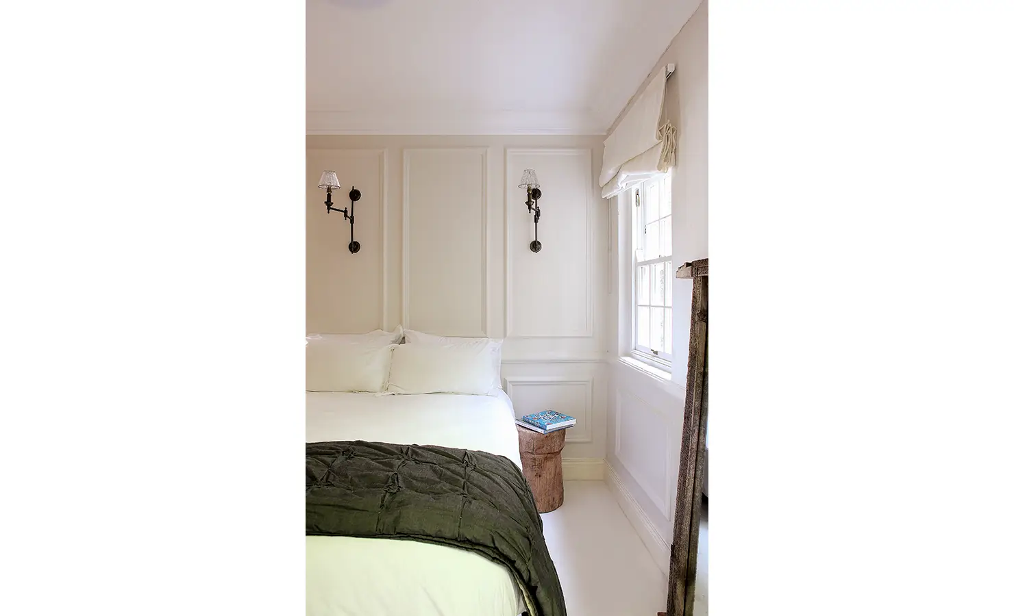 Perfect Hideaways: Soft neutral-toned bedroom with crisp white bedding, black metal sconces, and sunlight streaming in through a Roman-blinded window. Pepper Tree House, De Waterkant.
