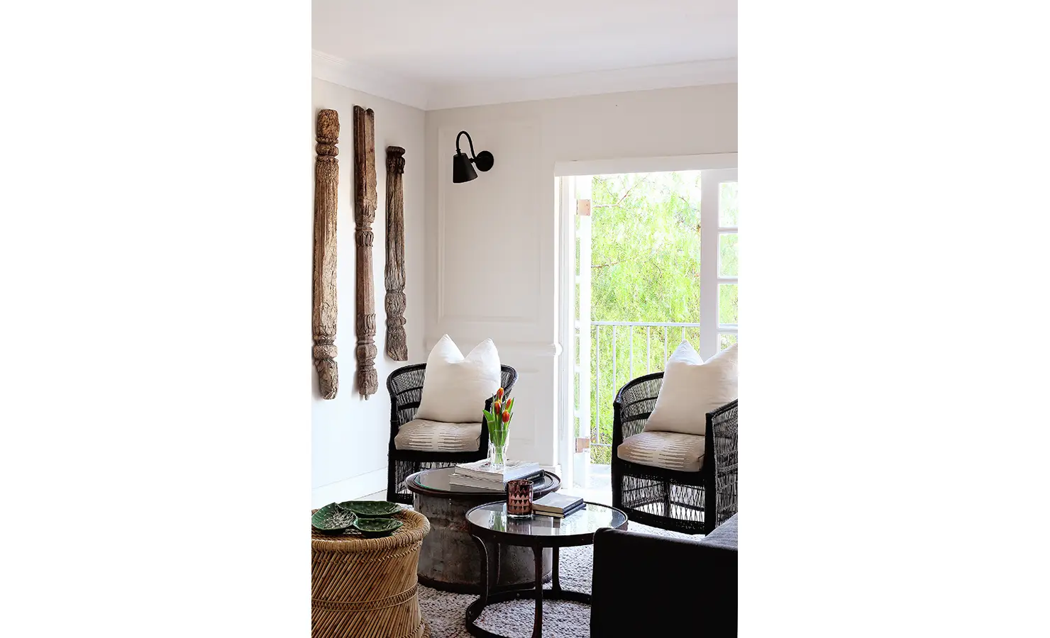 Perfect Hideaways: Cosy corner with woven armchairs, layered neutral cushions, and eclectic coffee tables beside rustic carved wood wall art and leafy views through French doors. Pepper Tree House, De Waterkant.