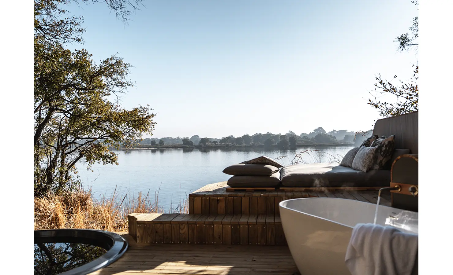 Perfect Hideaways: A luxurious open-air bathroom deck featuring a freestanding bathtub, plush seating, and a river-facing plunge pool, creating the ultimate private retreat in the African wilderness. Victoria Falls River Lodge, Zambezi National Park.