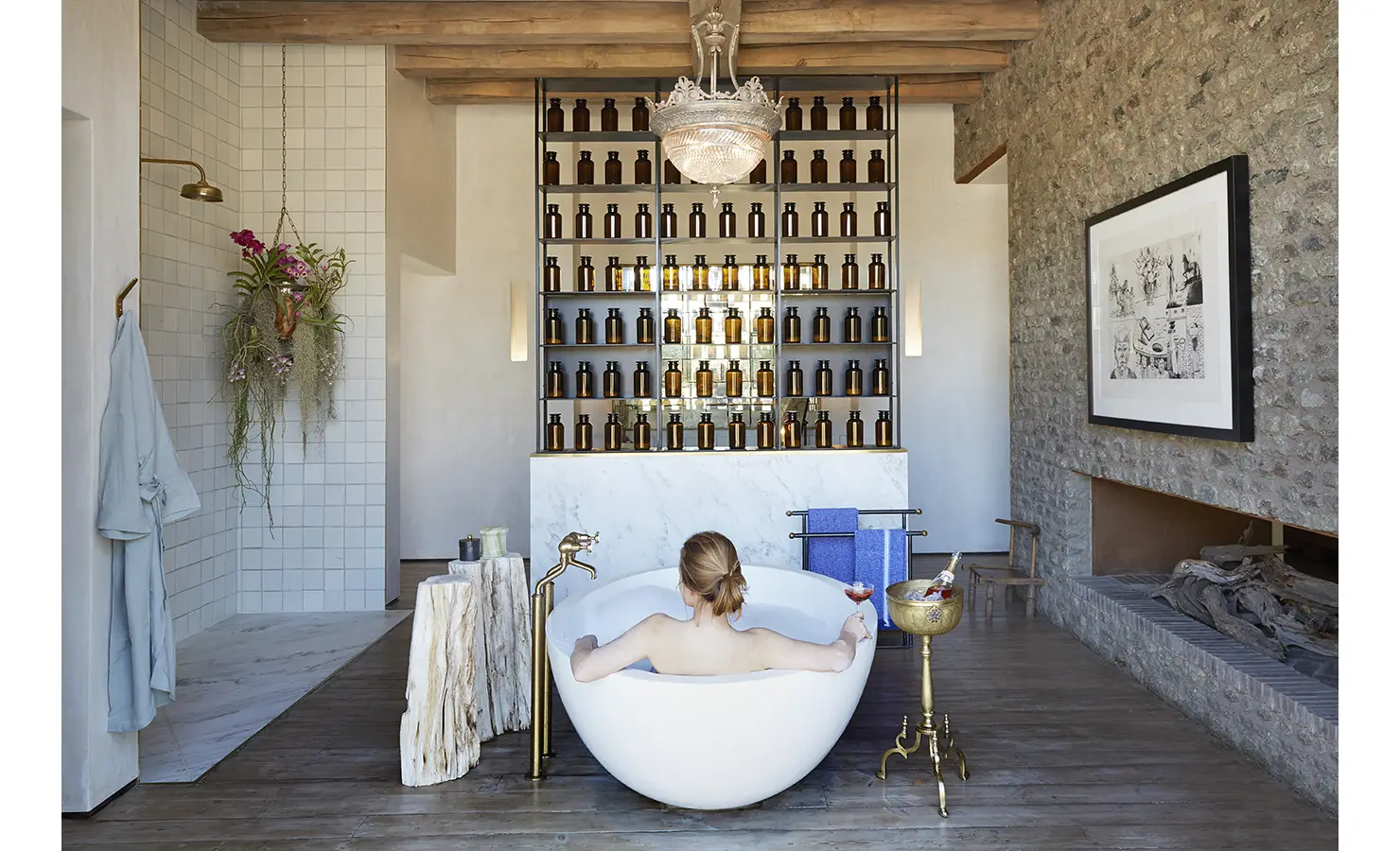 Perfect Hideaways: A lavish bathroom featuring a freestanding white bathtub with a gold faucet, an elegant chandelier, and a backdrop of shelves filled with decorative amber bottles. Kubili House, Thornybush Game Reserve.
