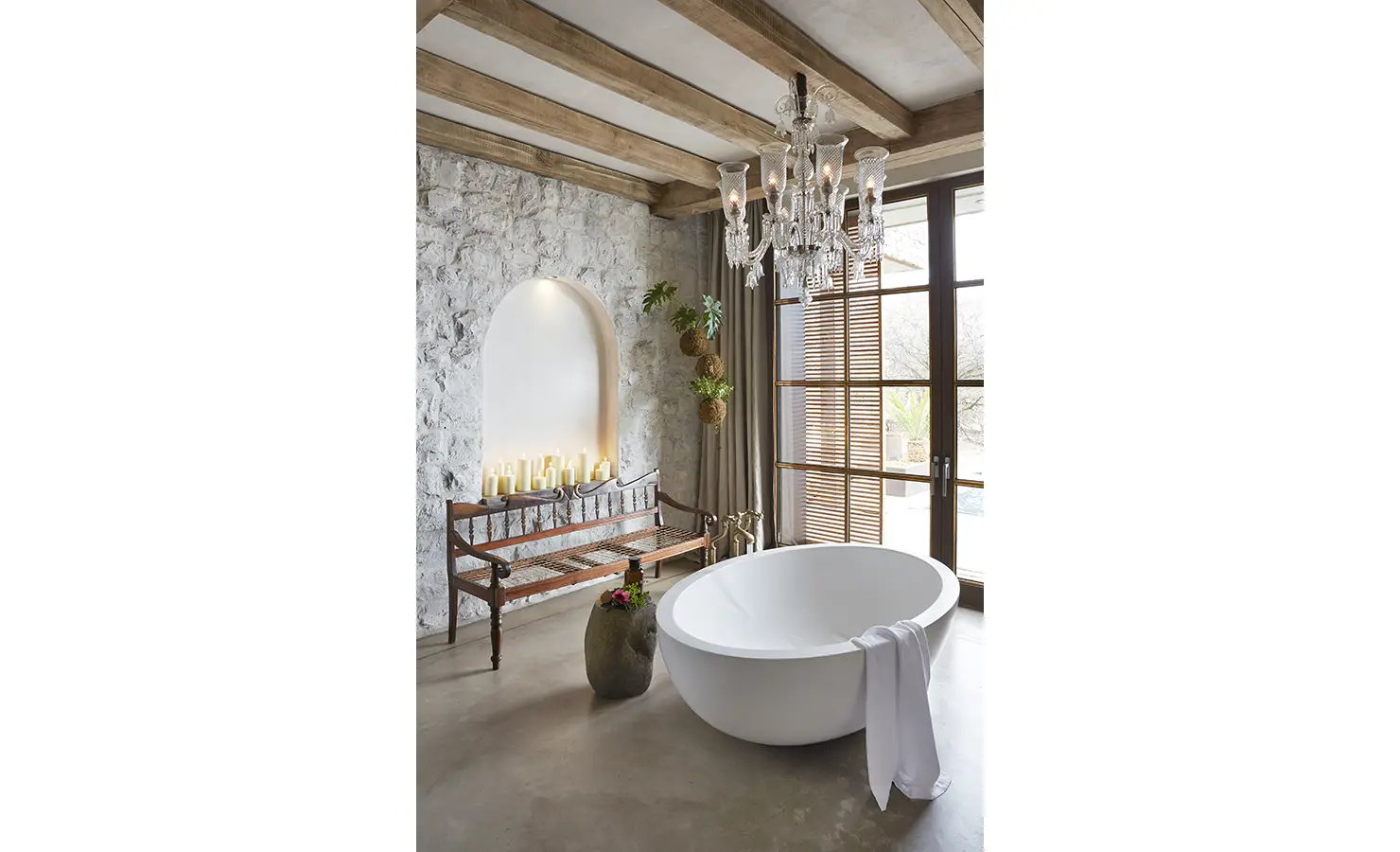Perfect Hideaways: A spa-inspired bathroom with a round soaking tub, soft lighting from a crystal chandelier, and a rustic bench with candles arranged in an alcove. Kubili House, Thornybush Game Reserve.