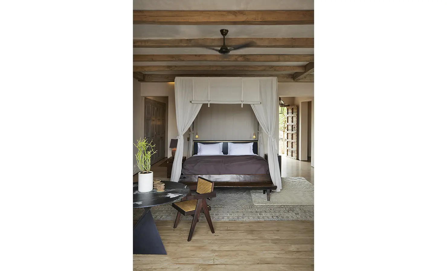 Perfect Hideaways: A sophisticated bedroom with a minimalist design, showcasing a four-poster bed with light drapes, a woven chair, and natural wood finishes. Kubili House, Thornybush Game Reserve.