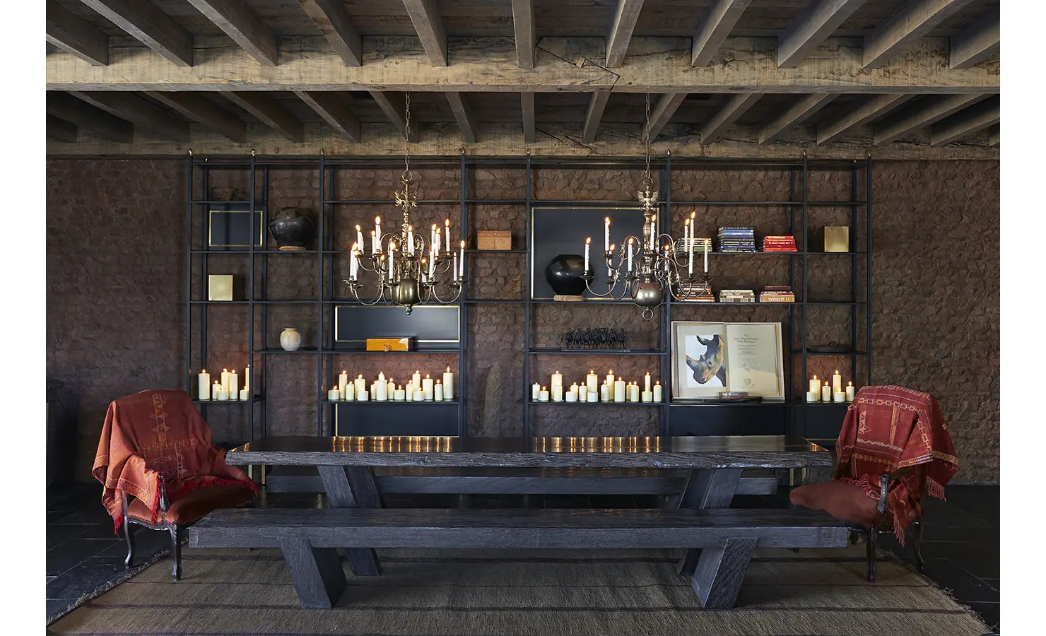 Perfect Hideaways: A cosy lounge area with dark wood furnishings, candelabras, and a backdrop of decorative shelves filled with candles, books, and sculptures. Kubili House, Thornybush Game Reserve.