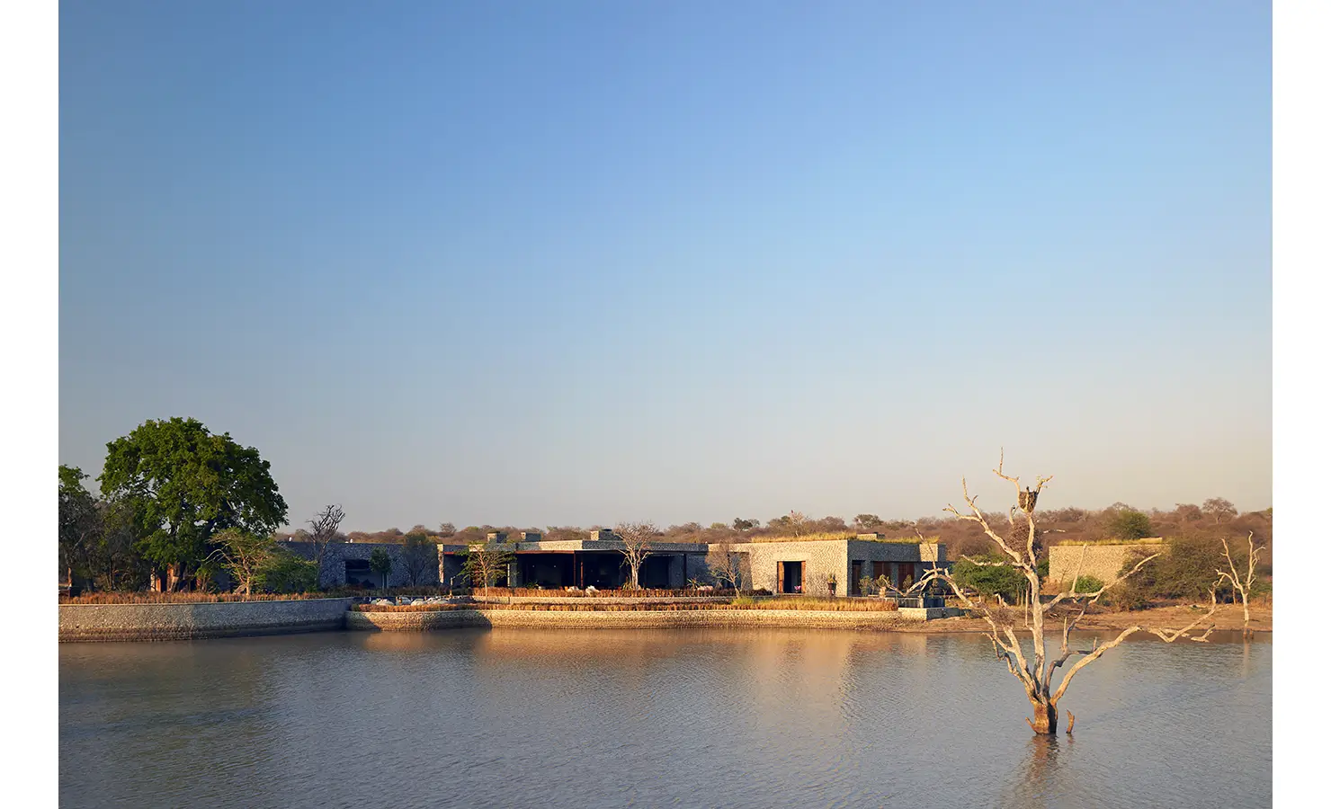 Perfect Hideaways: A panoramic view of the property nestled beside a calm river, showcasing stone structures and surrounding bushland under a clear blue sky. Kubili House, Thornybush Game Reserve.