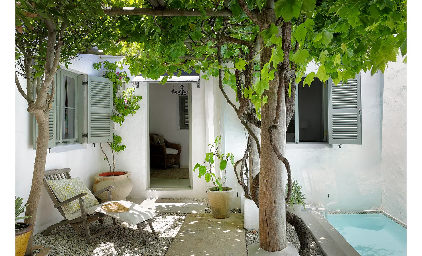 Perfect Hideaways: A charming courtyard with a grapevine-covered pergola, a small pool, and an inviting seating area with soft furnishings. Farniente, Kommetjie.